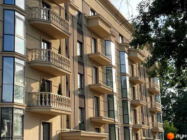 Фасад житлового комплексу Monaco з балконами та великими вікнами, оточений зеленню дерев.