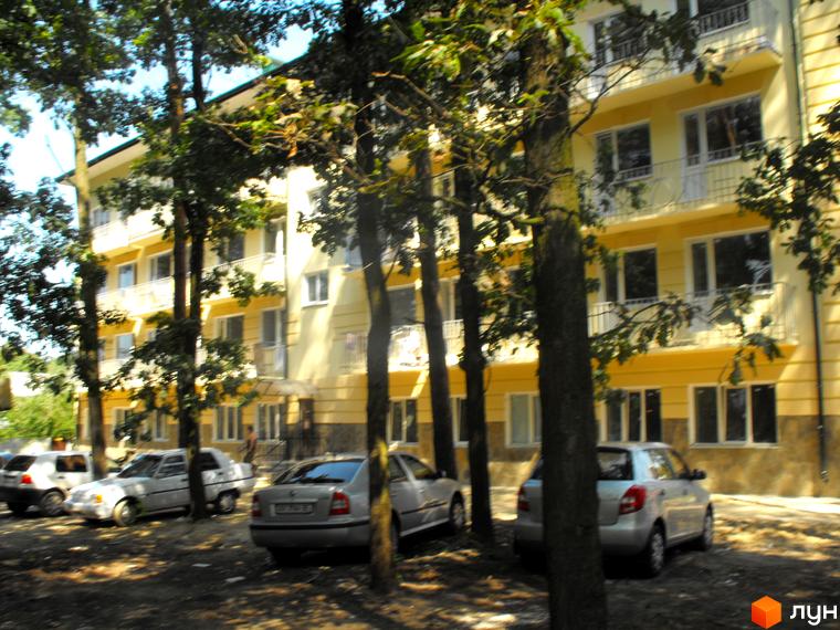 Зображення фасаду будинку по вул. Полтавська, 29. На передньому плані дерева та припарковані автомобілі.
