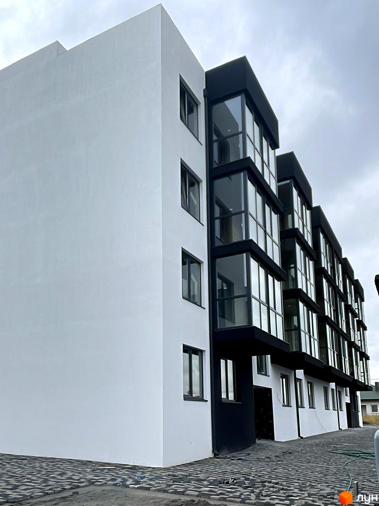 Житловий комплекс на вул. Фабрична з білим фасадом та чорними елементами скління. Територія перед будинком вимощена сірою бруківкою.