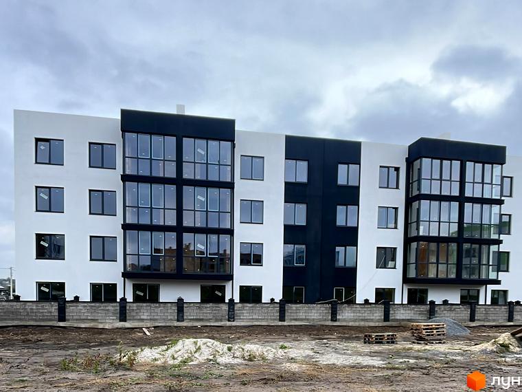 П'ятиповерховий житловий будинок з біло-чорним фасадом та великими вікнами. Перед будинком ґрунтова ділянка з огорожею та будматеріалами.