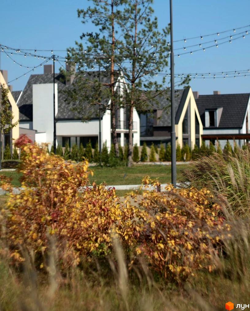 Котеджне містечко BELLAGIO: триповерхові будинки з темним дахом та великими вікнами, оточені зеленню та освітленням.