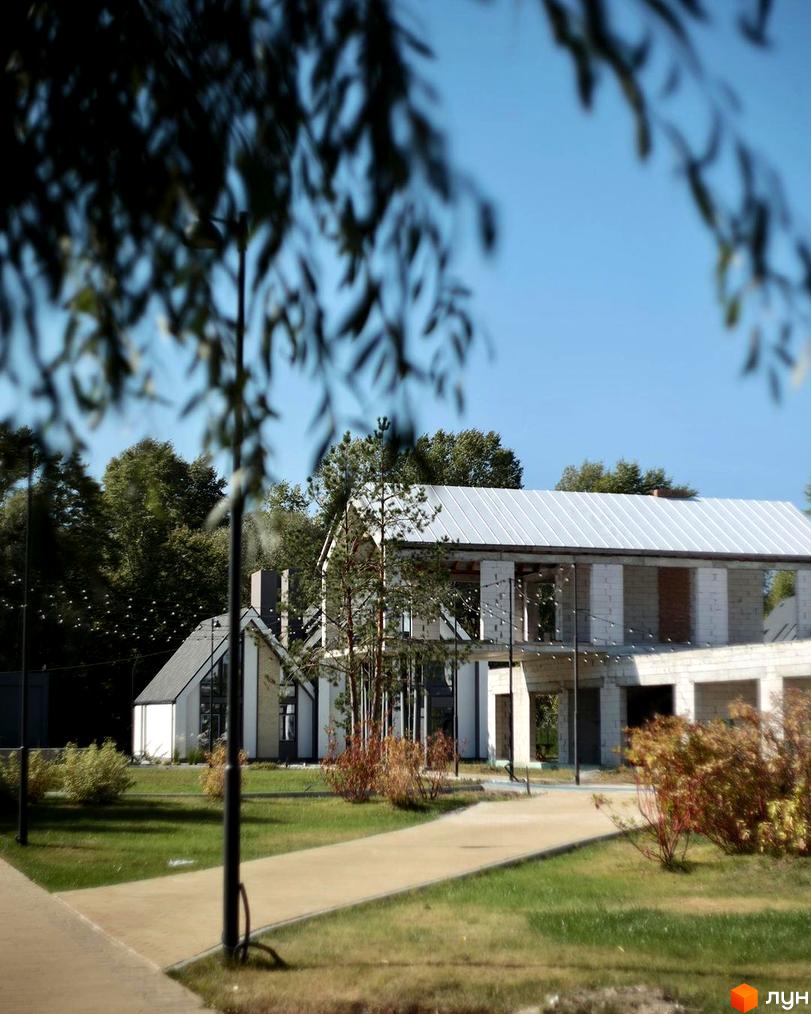 Зовнішній вигляд котеджного містечка BELLAGIO з дорогою та зеленими насадженнями. Новобудова з білої цегли та металевим дахом.