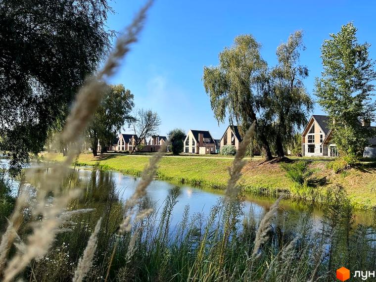 Котеджне містечко BELLAGGO: сучасні будинки з панорамними вікнами на березі річки. Зелена прибудинкова територія з деревами та травою.