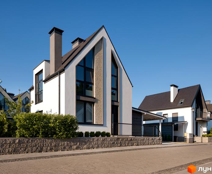 Котеджне містечко КМ VILLAGGO. Зовнішній вигляд будинків з білою штукатуркою, темними вікнами та цегляними вставками, з зеленими кущами та бруківкою.