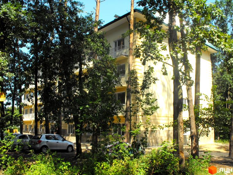 Зовнішній вигляд триповерхового будинку на вулиці Полтавській, 29. На території ростуть дерева та кущі, припарковані автомобілі.