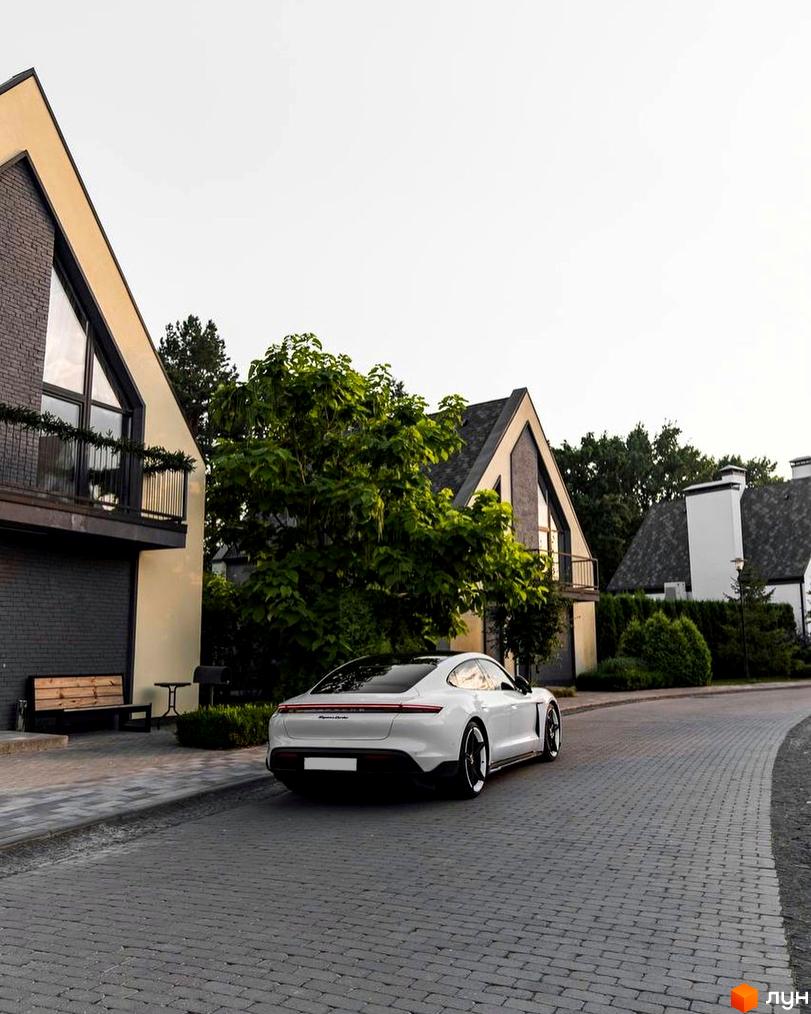 Котеджне містечко КМ VILLAGGO з білими фасадами та темними дахами, розташоване на бруківці з зеленою зоною та автомобілем.