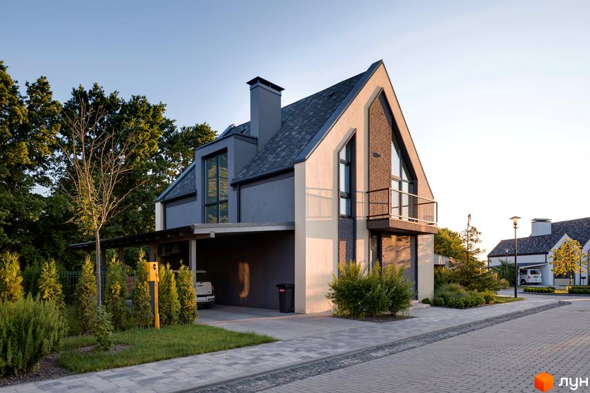 Котеджне містечко КМ VILLAGGO. Фасад будинку з сірою черепицею та цегляними вставками, прибудинкова територія з деревами та бруківкою.