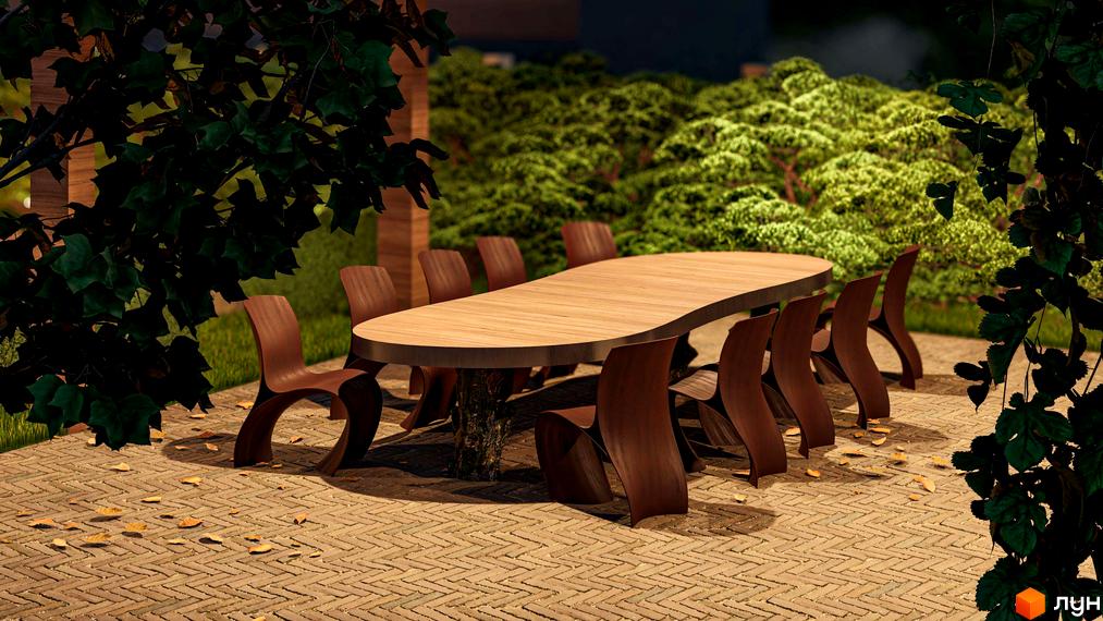 Прибудинкова територія Житлового комплексу Минай з облаштованою зоною відпочинку: довгий дерев'яний стіл та стільці на брукованій терасі серед зелені.