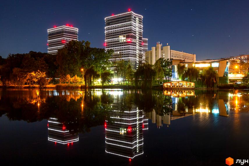 Житловий комплекс White Lines біля озера вночі. Високі будинки з підсвіткою відбиваються у воді, створюючи красиву атмосферу.