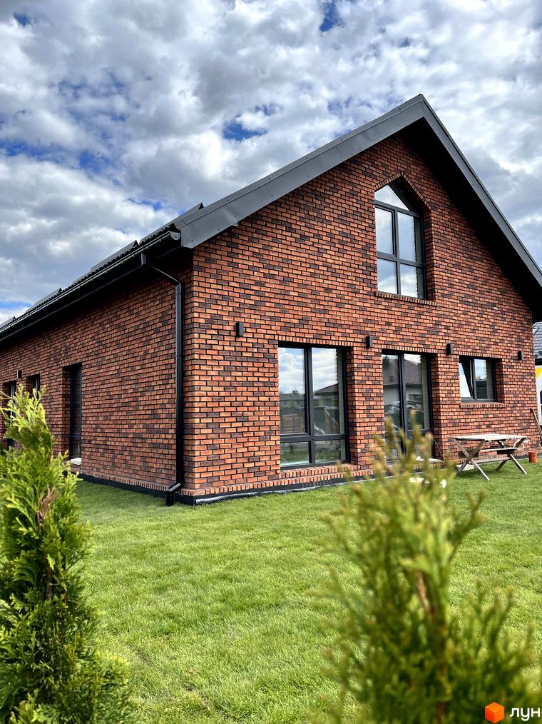 Цегляний будинок в Котеджному містечку Південна Баварія з великими вікнами та доглянутою прибудинковою територією з газоном та деревами.