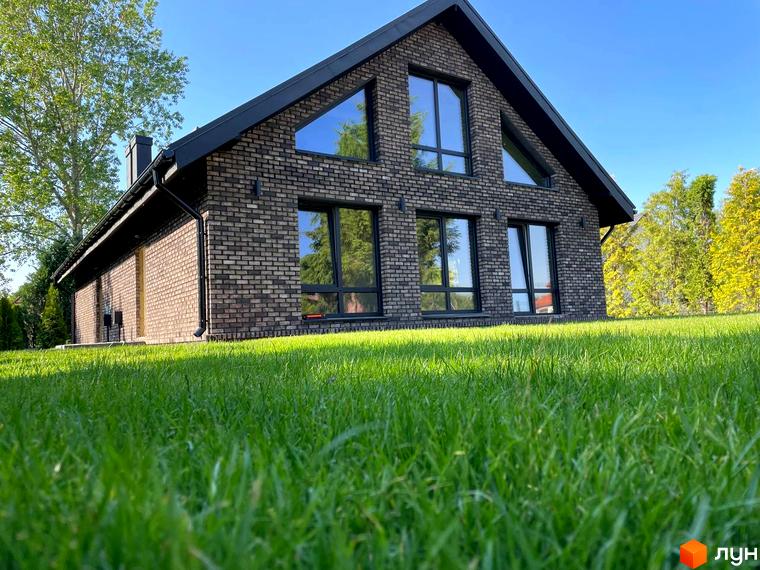 Цегляний будинок з великими вікнами на тлі зеленої трави. Котеджне містечко Південна Баварія - ідеальне місце для вашого життя.