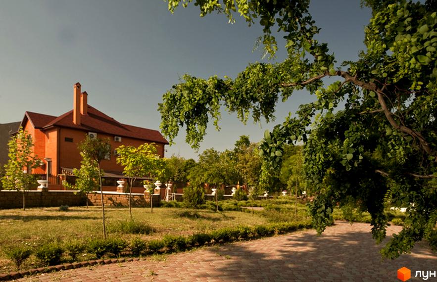 Вигляд будинку в Котеджному містечку Сосновий берег. Навколо зелена прибудинкова територія з доріжками та деревами.