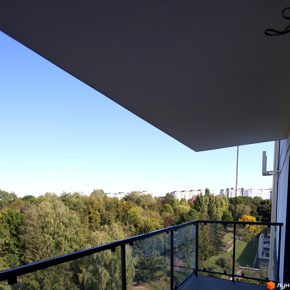 Вид з балкону на дерева та міські будівлі у Житловому комплексі SOURENZH. На передньому плані скляна огорожа балкону.