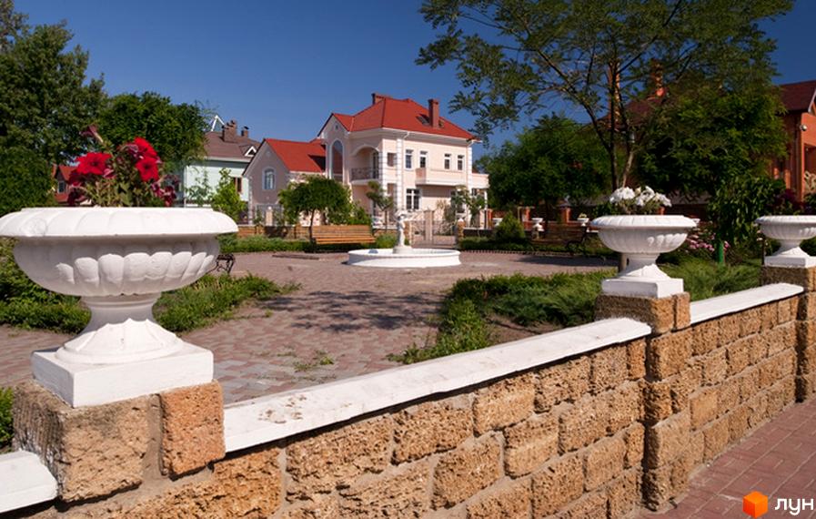 Житловий район Сосновий берег: двоповерховий будинок з червоним дахом, ландшафтний дизайн з клумбами та фонтаном.