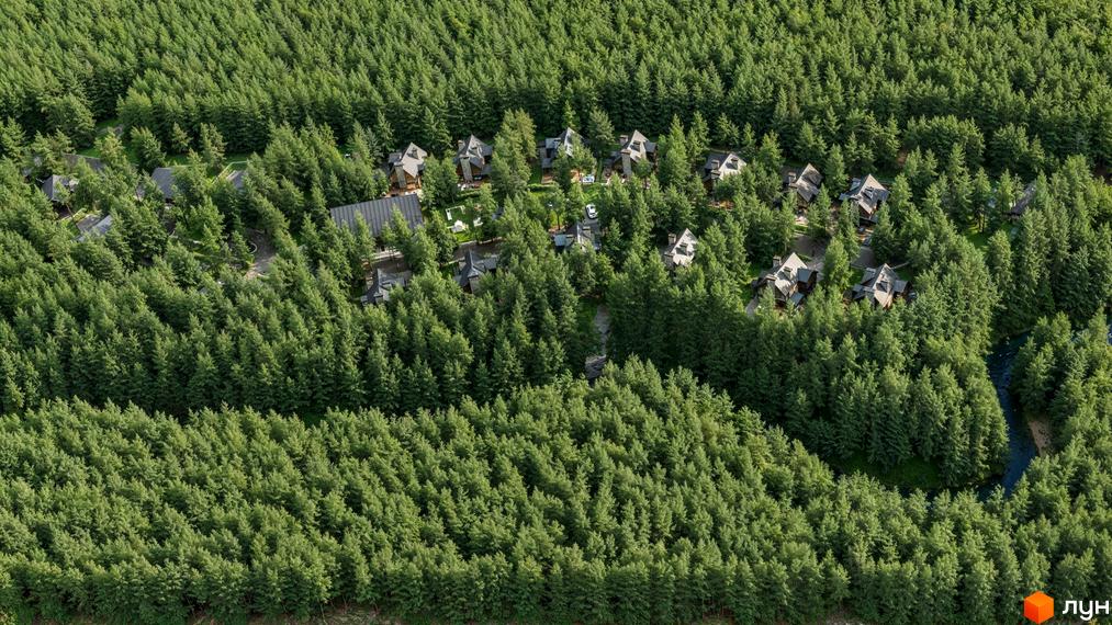 Вид зверху на дахи будинків серед зеленого лісу в Житловому районі Guta Nova. Навколо будівель багато дерев.