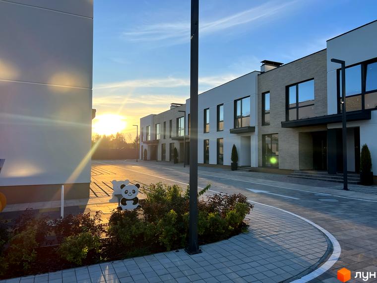 Таунхауси Soul City з білими фасадами та темними вікнами, розташовані вздовж вимощеної дороги. Територія має озеленення та дитячі фігурки.