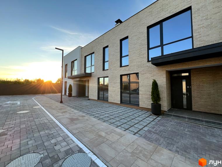 Таунхауси Soul City з цегляним фасадом та великими вікнами, розташовані на брукованій прибудинковій території.