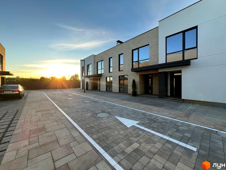 Таунхауси Soul City з великими вікнами та цегляним фасадом на тлі заходу сонця. Прибудинкова територія з бруківкою та парковкою.