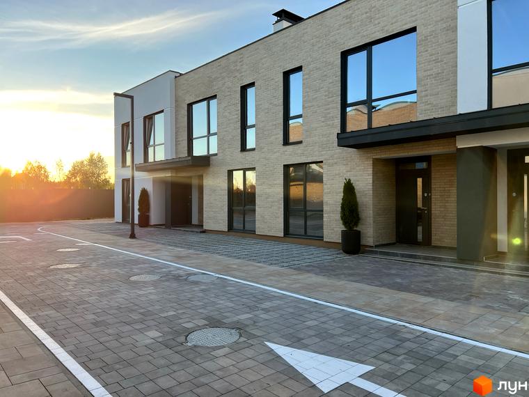 Будівля Котеджного містечка Soul City зі світлої цегли та великими темними вікнами. Перед будинком вимощена плиткою доріжка з білою розміткою.