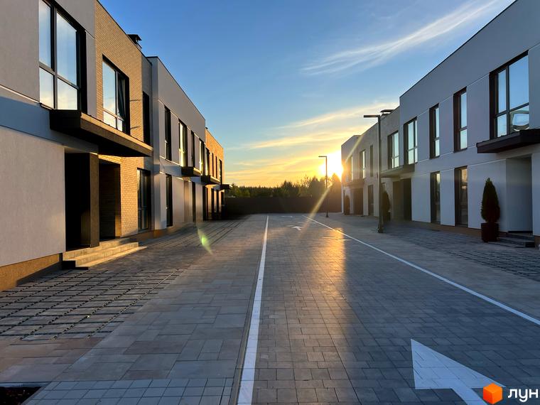 Таунхауси Soul City з цегляним та білим фасадом на тлі заходу сонця. Парковка перед будинками з бруківки з розміткою.