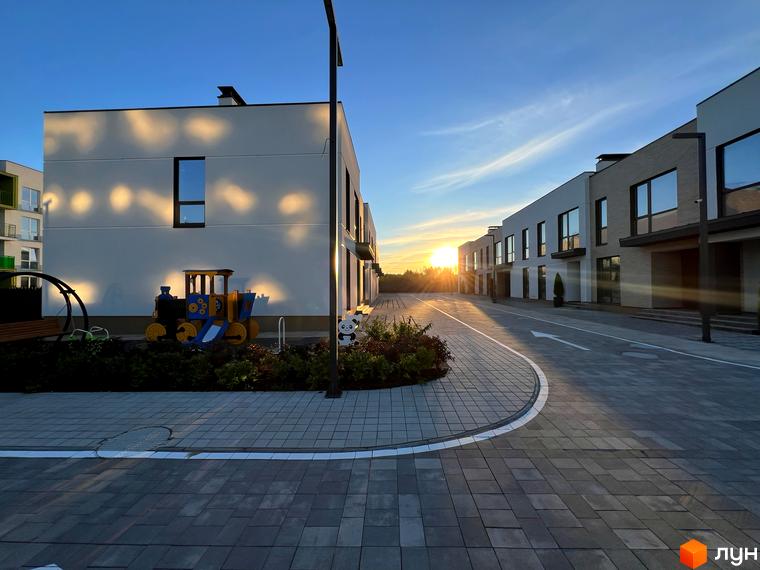 Таунхауси Soul City з дитячим майданчиком та дорогою біля будівель на фоні заходу сонця. Зовнішній вигляд будинків та прибудинкової території.