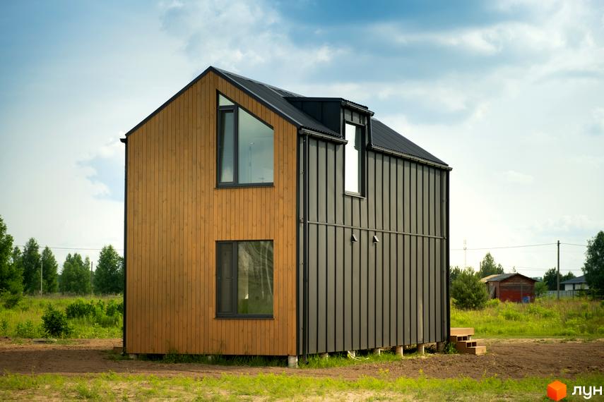 Котеджне містечко Залісся Village: двоповерховий будинок з дерев'яним та металевим фасадом, розташований на зеленій ділянці з деревами.