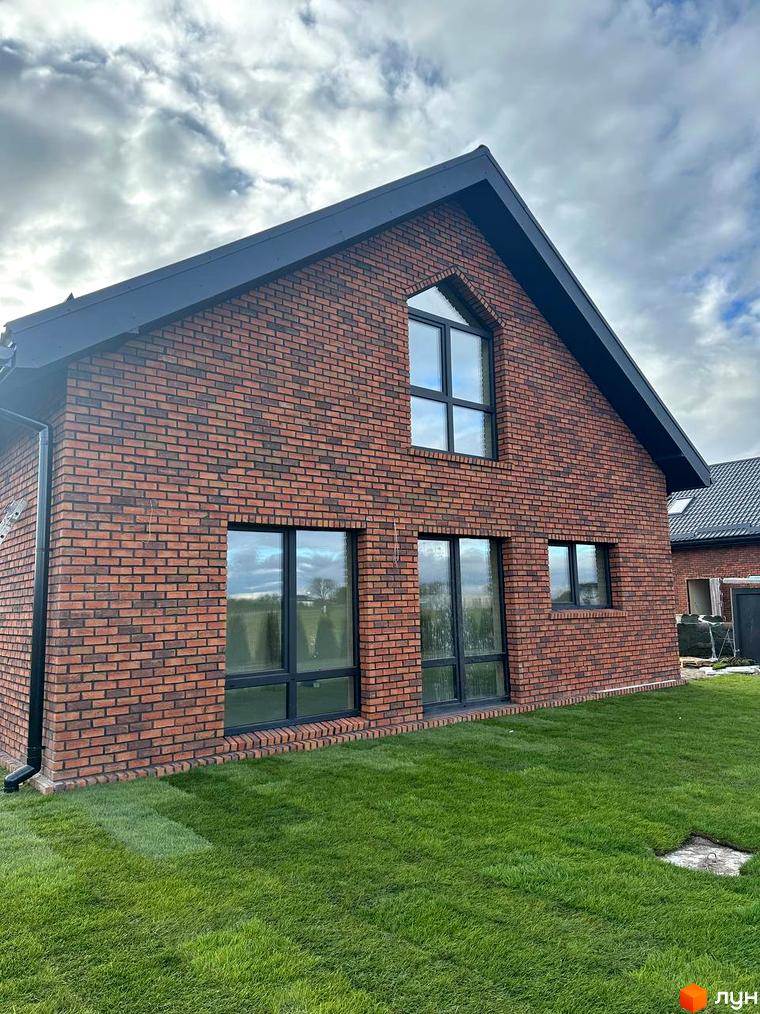 Вигляд цегляного будинку в Котеджному містечку Одноповерховий Київ - Зубра. Навколо будинку зелений газон.