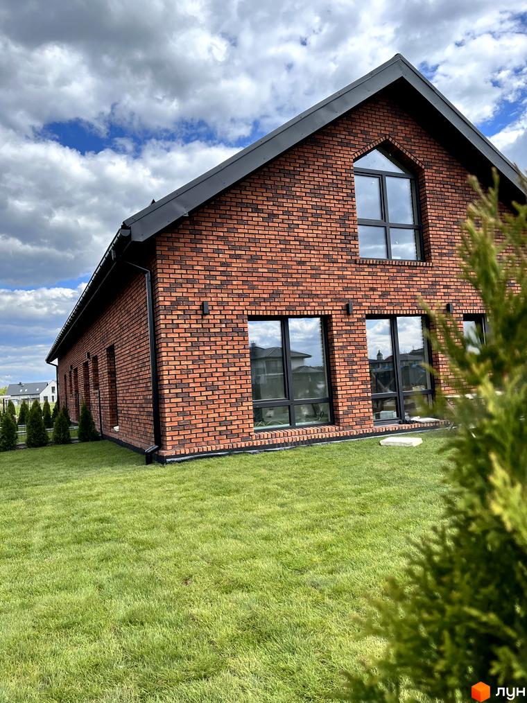 Зображення будинку з червоної цегли з великими вікнами в Котеджному містечку Одноповерховий Київ - Зубра. Зелений газон перед будинком.