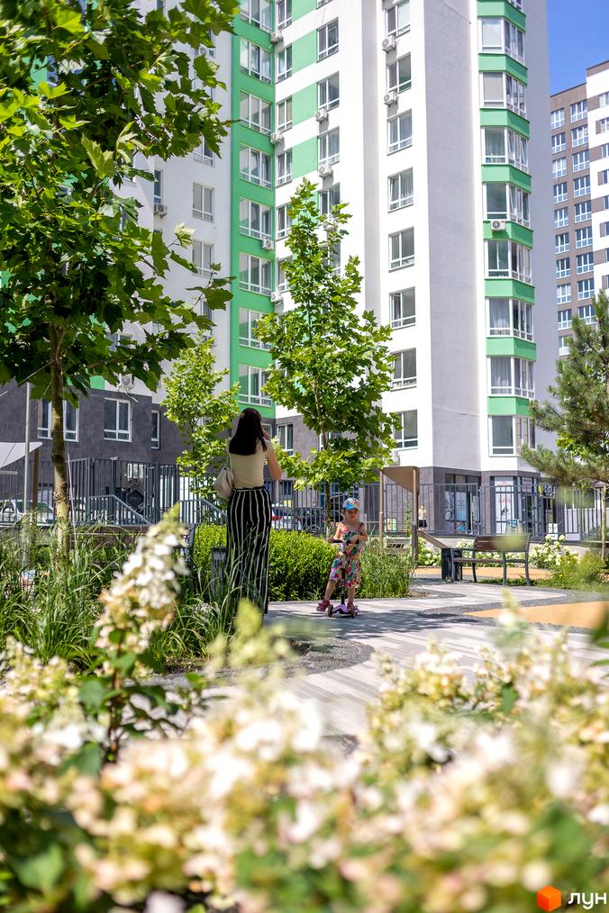 Зовнішній вигляд житлового комплексу City Park з зеленими та білими фасадами. На прибудинковій території граються діти на самокатах.