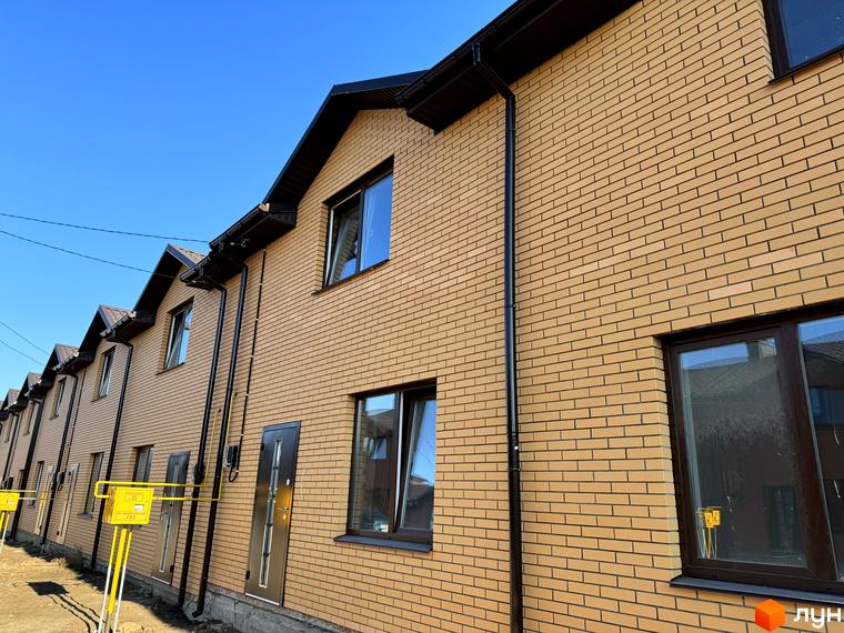 Зовнішній вигляд Котеджного містечка Весняний з жовтої цегли з темними вікнами та дахом. На передньому плані жовта газова труба.