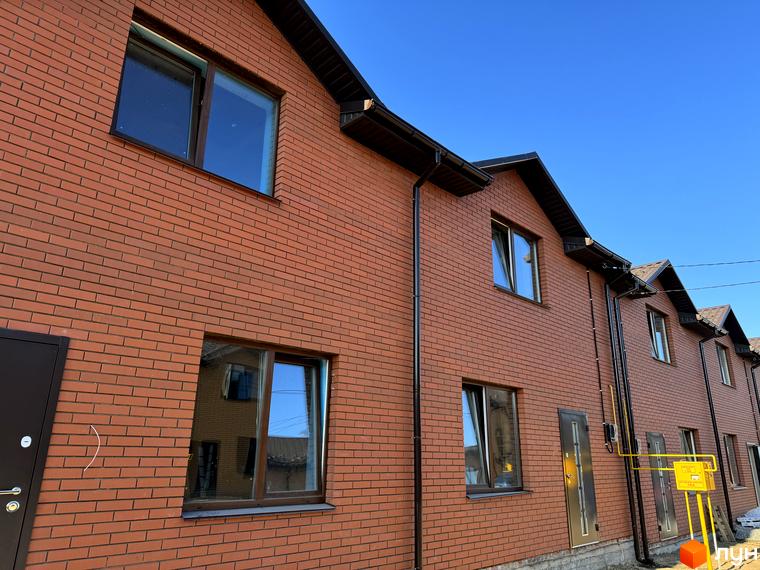 Ряд котеджів Котеджного містечка Весняний з червоної цегли та коричневими вікнами. На фасаді видно водостічні труби та газові комунікації.