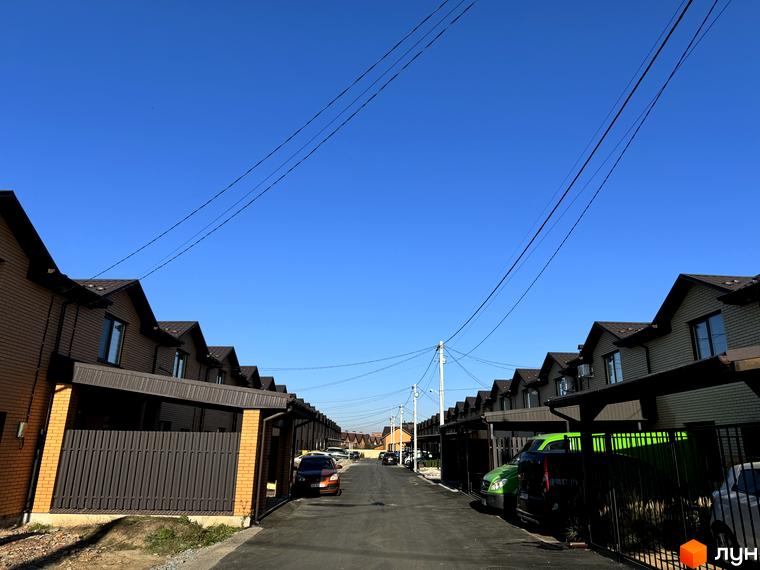 Котеджне містечко Весняний: Ряд двоповерхових котеджів з коричневої цегли та темними дахами, вздовж вулиці з прибудинковими ділянками.