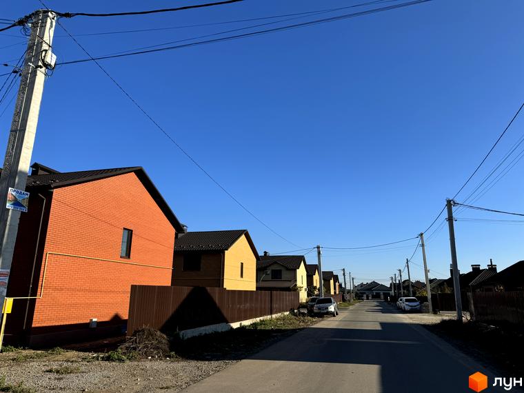 Вигляд будинків у Котеджному містечку Весняний. Цегляні та дерев'яні будинки з темними дахами вздовж асфальтованої дороги.