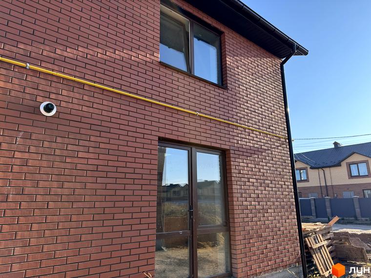 Зовнішній вигляд будинку з червоної цегли в Котеджному містечку Весняний. На стіні видно трубу газопостачання та камеру відеоспостереження.