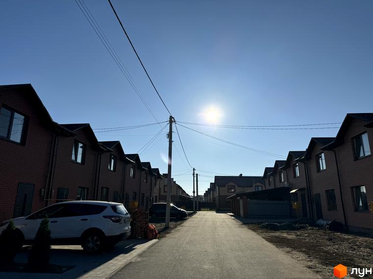 Ряд двоповерхових коричневих цегляних будинків Котеджного містечка Весняний вздовж вулиці з припаркованим авто під яскравим сонцем.