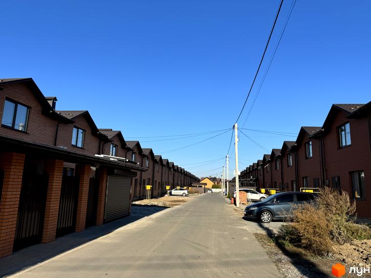 Ряди цегляних котеджів з темними дахами у Котеджному містечку Весняний. Вулиця з припаркованими автомобілями.