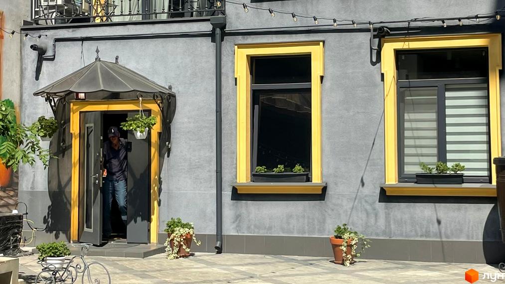 Зовнішній вигляд фасаду житлового комплексу Вентімілья з жовтими віконними рамами та вхідною групою. Прибудинкова територія з рослинами в горщиках.