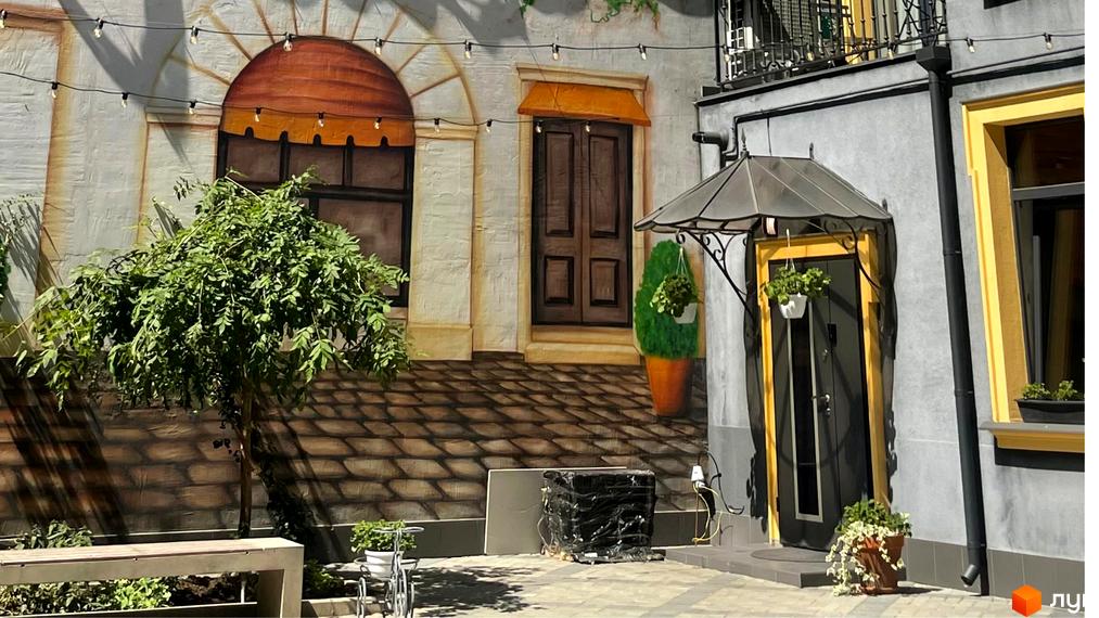 Житловий комплекс Вентімілья: фасад будинку з вікнами та дверима, прибудинкова територія з деревом та лавкою.