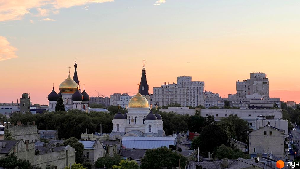 Вид на місто з храмом із золотими куполами та житловими будинками на тлі вечірнього неба. Загальний план оточення Новобудови Гімназист.