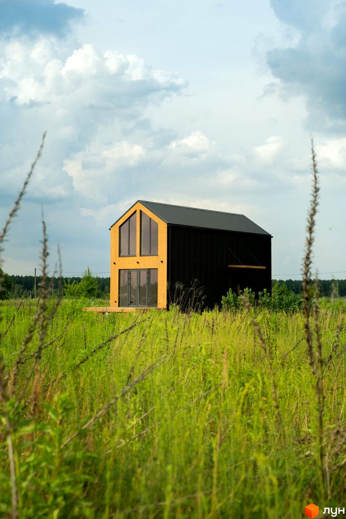 Сучасний двоповерховий будинок з чорним фасадом та великими вікнами, розташований серед зеленої трави.