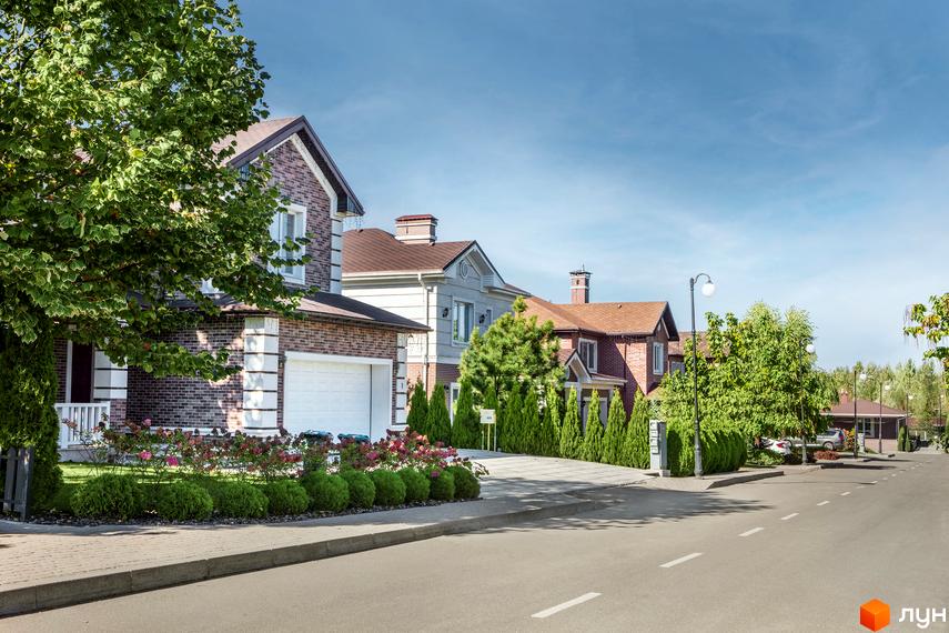 Зображення сторінки житлового комплексу КМ Green Hills. Цегляні будинки з гаражами, озеленена прибудинкова територія та асфальтована дорога.