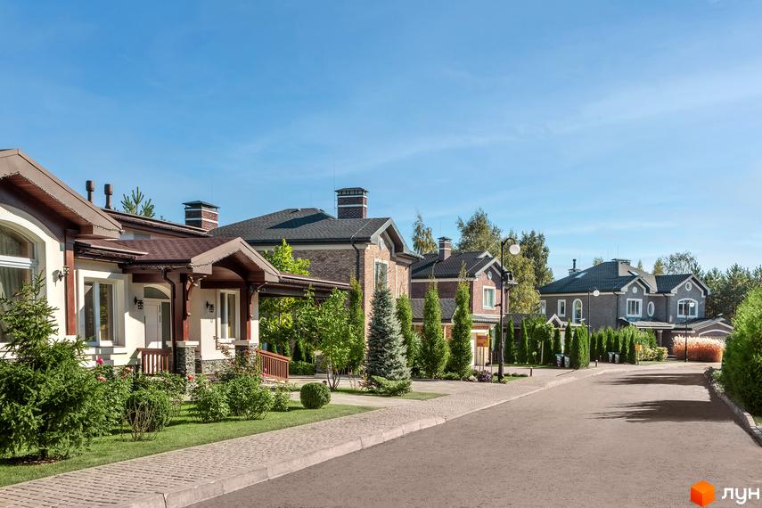 Зображення сторінки житлового комплексу КМ Green Hills. На фото видно будинки з коричневими дахами та світлими фасадами. Перед будинками доглянута прибудинкова територія з газонами та деревами.