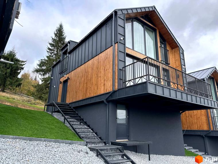 Сучасний будинок FOMICH RESIDENCE GUESTHOUSES з дерев'яними та металевими елементами фасаду, розташований на схилі з доглянутим газоном та гравійною доріжкою.