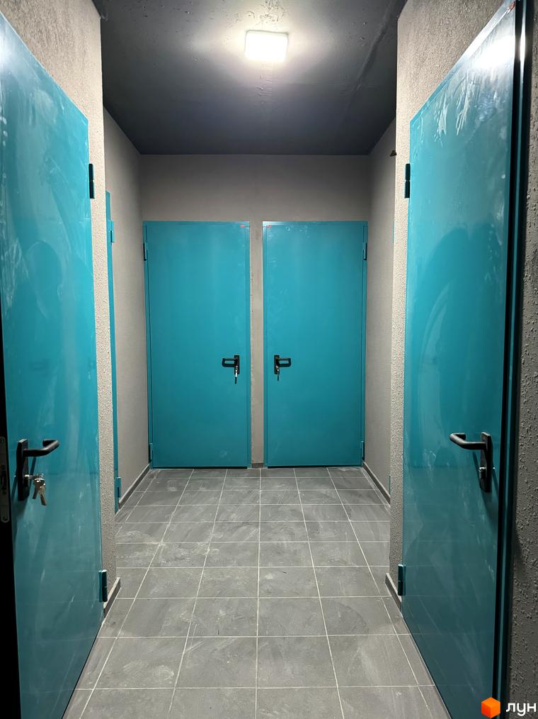Житловий комплекс Буковинська 20А. Коридор з бірюзовими дверима та сірою плиткою на підлозі.