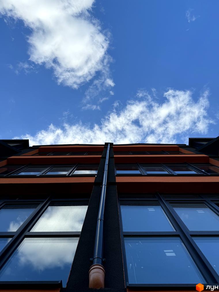 Буковинська 20А - це новобудова з панорамними вікнами та цегляним фасадом, що виходить на блакитне небо з хмарами.