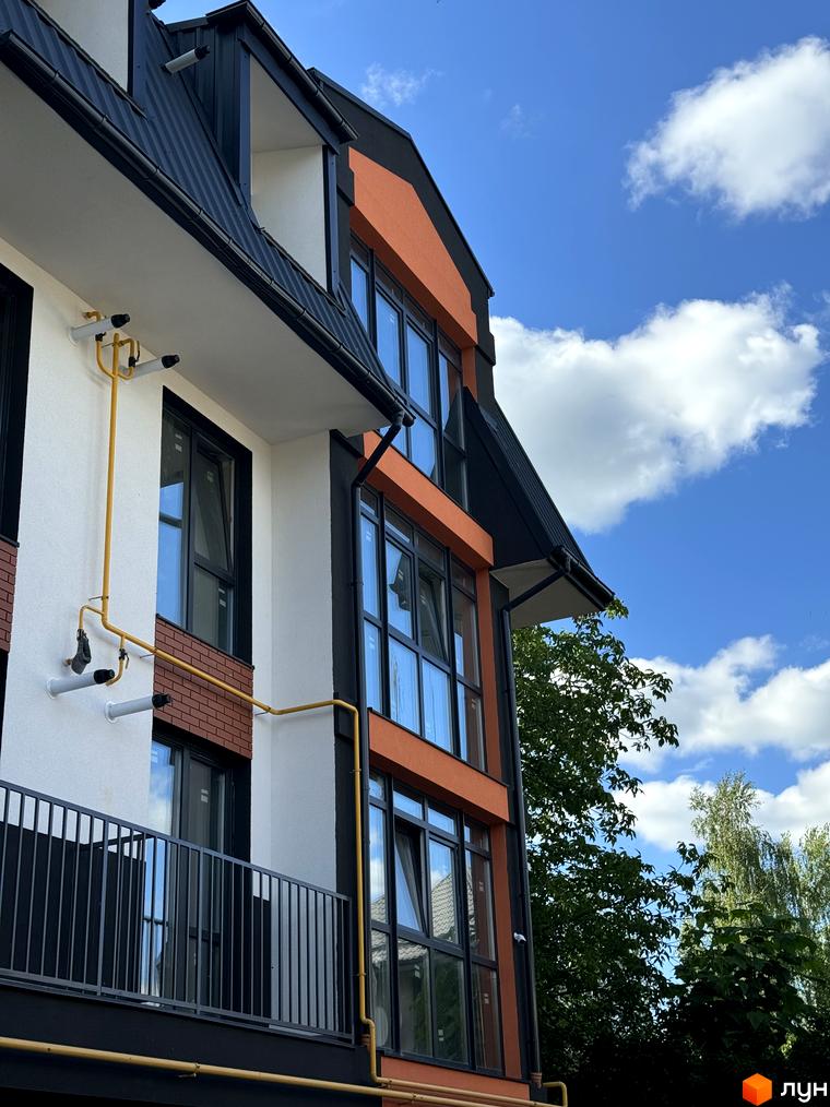 Фасад житлового комплексу Буковинська 20А з панорамними вікнами та балконами на тлі блакитного неба з хмарами. Зелені дерева оточують будівлю.