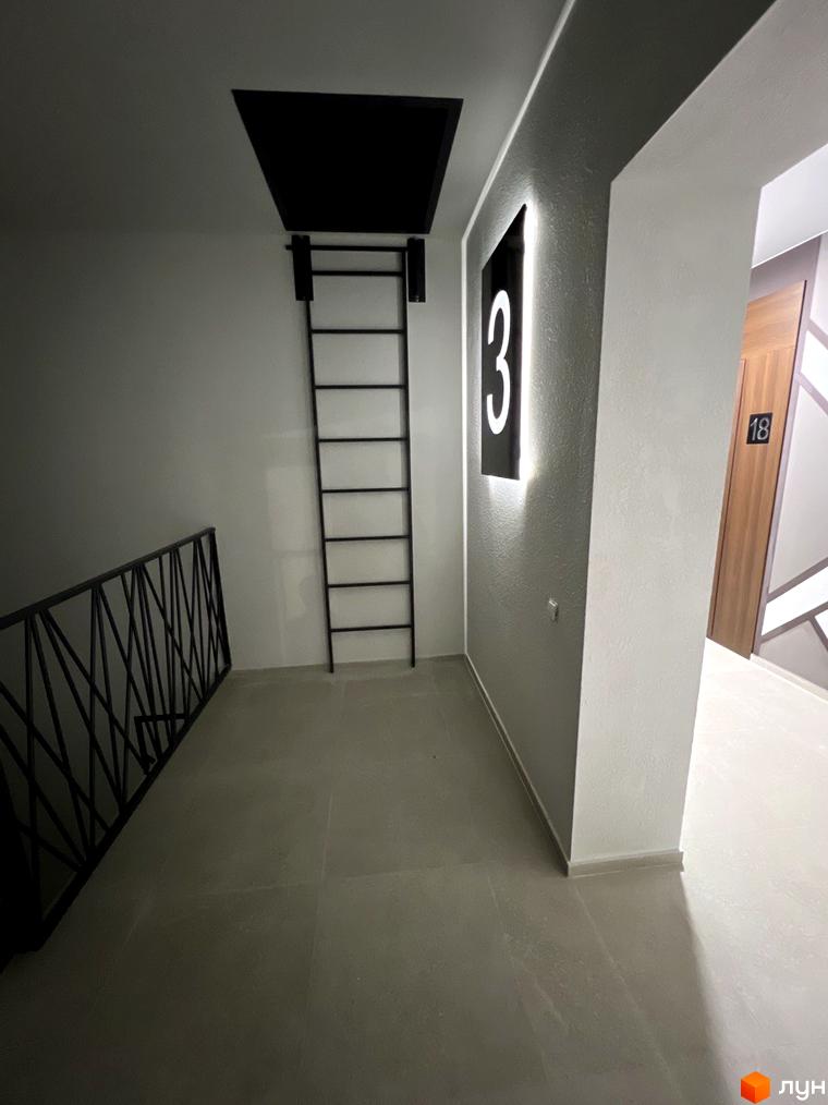 Будівельний проєкт Буковинська 20А: сходова клітка з чорними перилами та декоративною підсвіткою номера 3, поруч двері з номером 18.