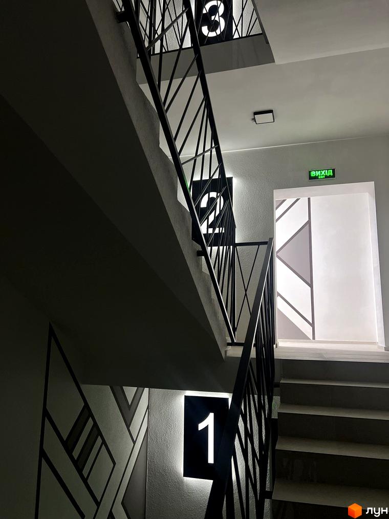 Сходи в житловому комплексі Буковинська 20А з підсвіченими номерами поверхів та виходом. Сучасний дизайн сходів та дверей.