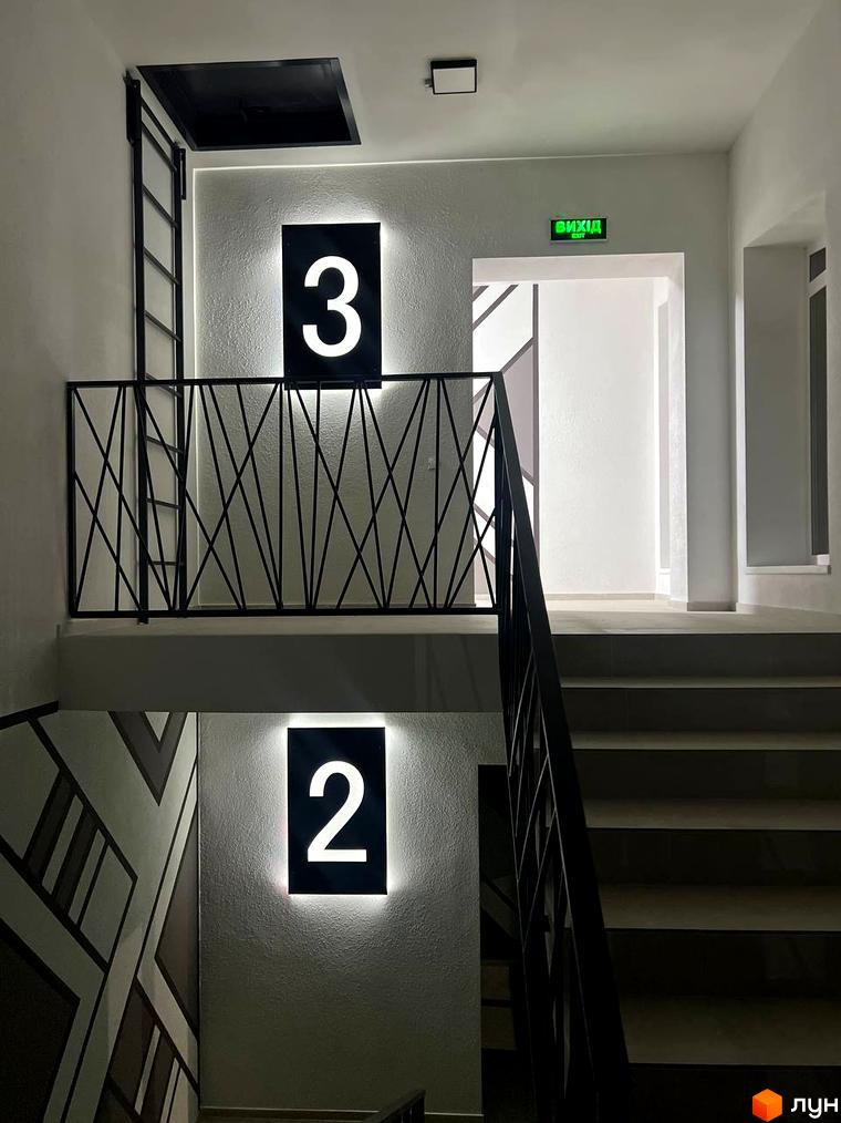 Сходи в житловому комплексі Буковинська 20А з підсвіченими номерами поверхів 2 та 3. На стіні видно геометричний візерунок.