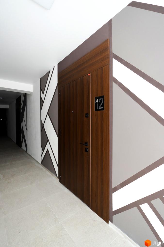 Будинок ЖК Буковинська 20А з дерев'яними дверима та геометричним візерунком на стінах. Сучасний коридор з плитковою підлогою.